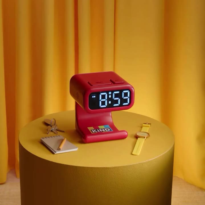 A red KIND Bar Alarm on a yellow table with a KIND bar beneath its display